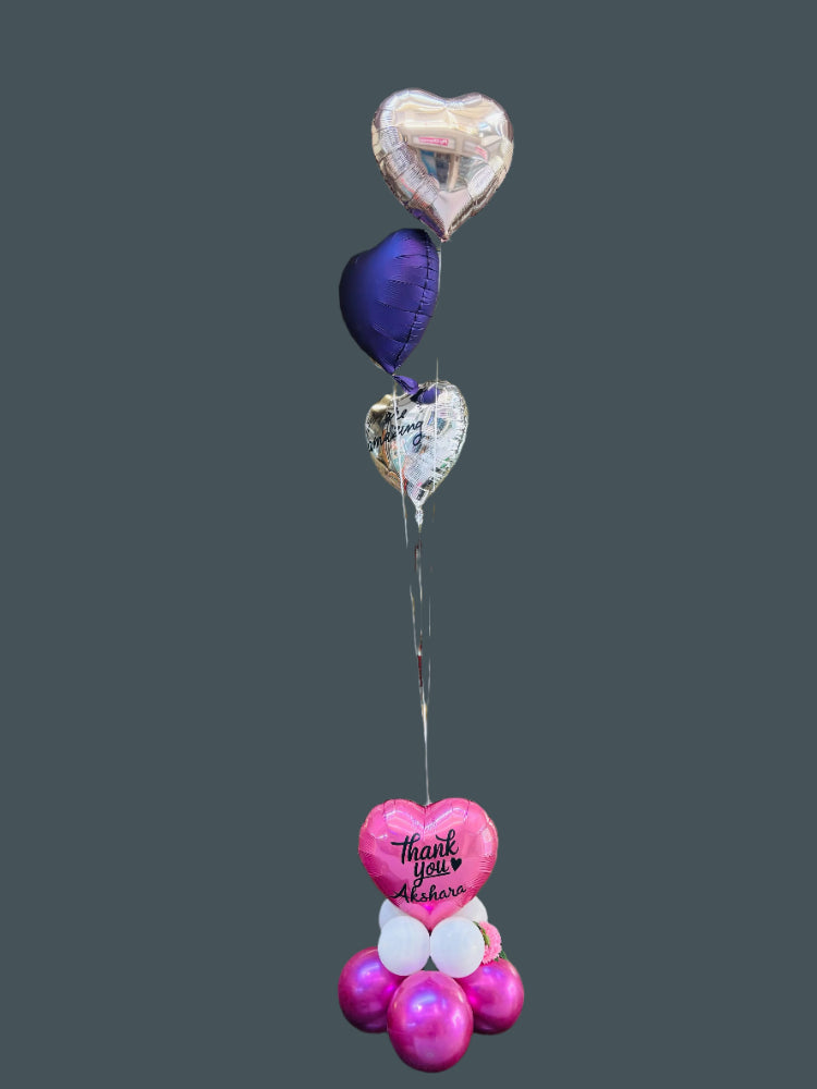 A beautifully arranged bouquet of helium balloons featuring a central metallic balloon with the words &quot;Thank You&quot; in elegant script, surrounded by coordinating pastel and metallic balloons in shades of gold, white, and blush pink, tied together with satin ribbons and displayed against a soft, neutral background.