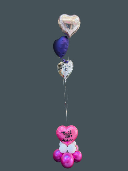A beautifully arranged bouquet of helium balloons featuring a central metallic balloon with the words &quot;Thank You&quot; in elegant script, surrounded by coordinating pastel and metallic balloons in shades of gold, white, and blush pink, tied together with satin ribbons and displayed against a soft, neutral background.