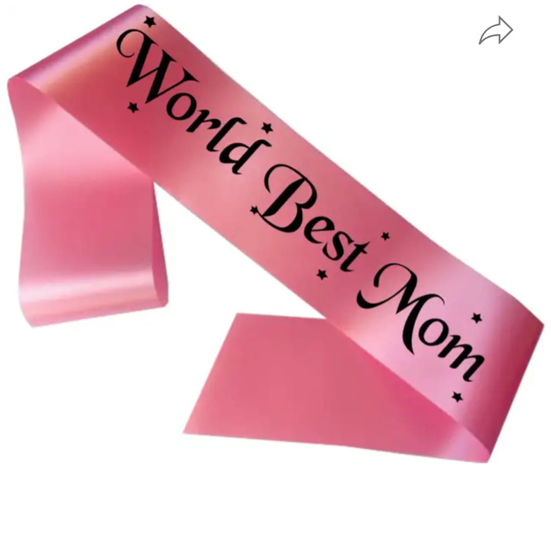 Mother’s Day sash: soft pink satin ribbon with ‘World Best Mom’ in elegant gold script, draped over a gift box with floral accents
